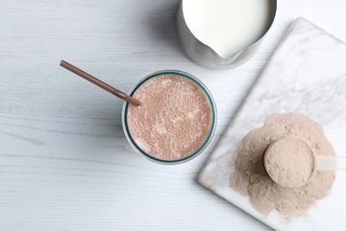 Photo of Glass with protein shake, jug of milk and powder on white wooden table, top view