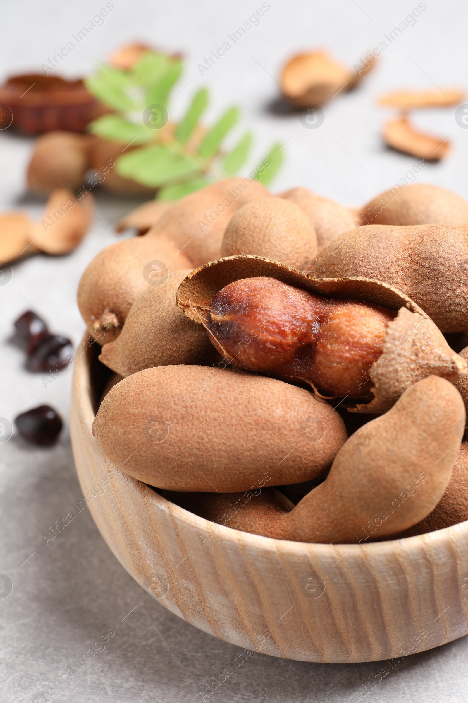 Photo of Delicious ripe tamarinds in wooden bowl on light table, closeup