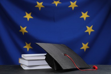 Photo of Graduation cap and books on black table against flag of European Union
