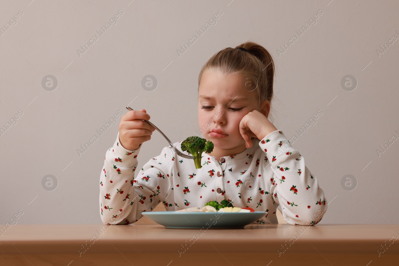 Photo of Cute little girl refusing to eat her dinner at table on grey background