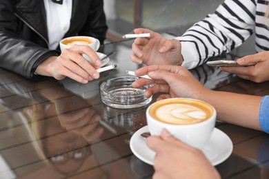 Women holding cigarettes over glass ashtray at table, closeup