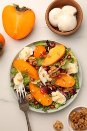 Photo of Delicious persimmon salad with cheese and pomegranate served on white table, flat lay