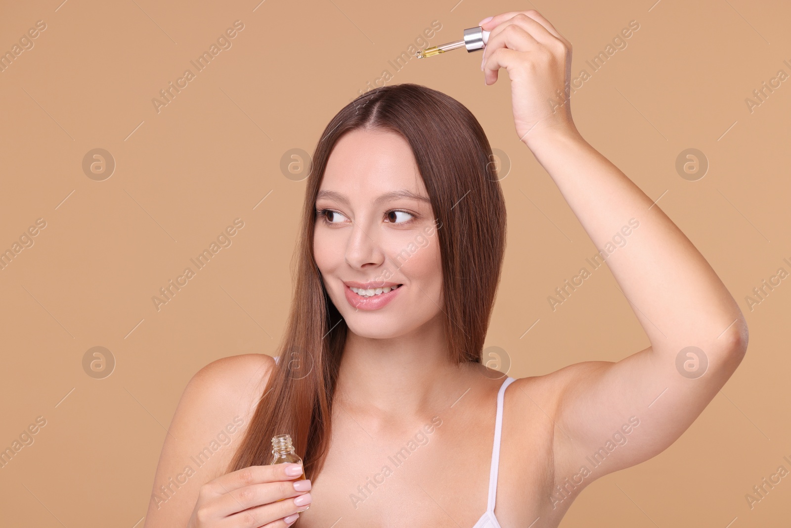 Photo of Beautiful woman applying serum onto hair on beige background