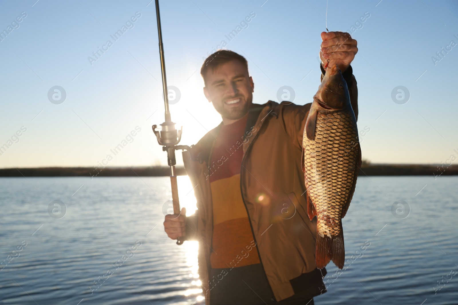 Photo of Fisherman holding rod and catch at riverside, focus on fish