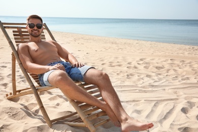 Photo of Young man relaxing in deck chair on sandy beach