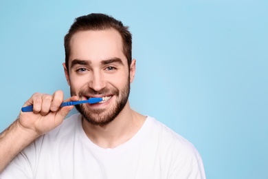 Young man brushing his teeth on grey background