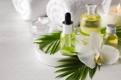 Essential oils, orchid flower and green leaves on white table, closeup