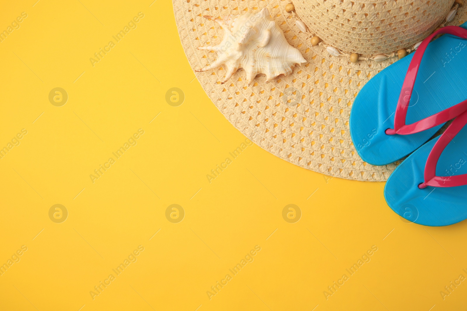 Photo of Flip flops, hat and seashell on yellow background, flat lay. Beach accessories