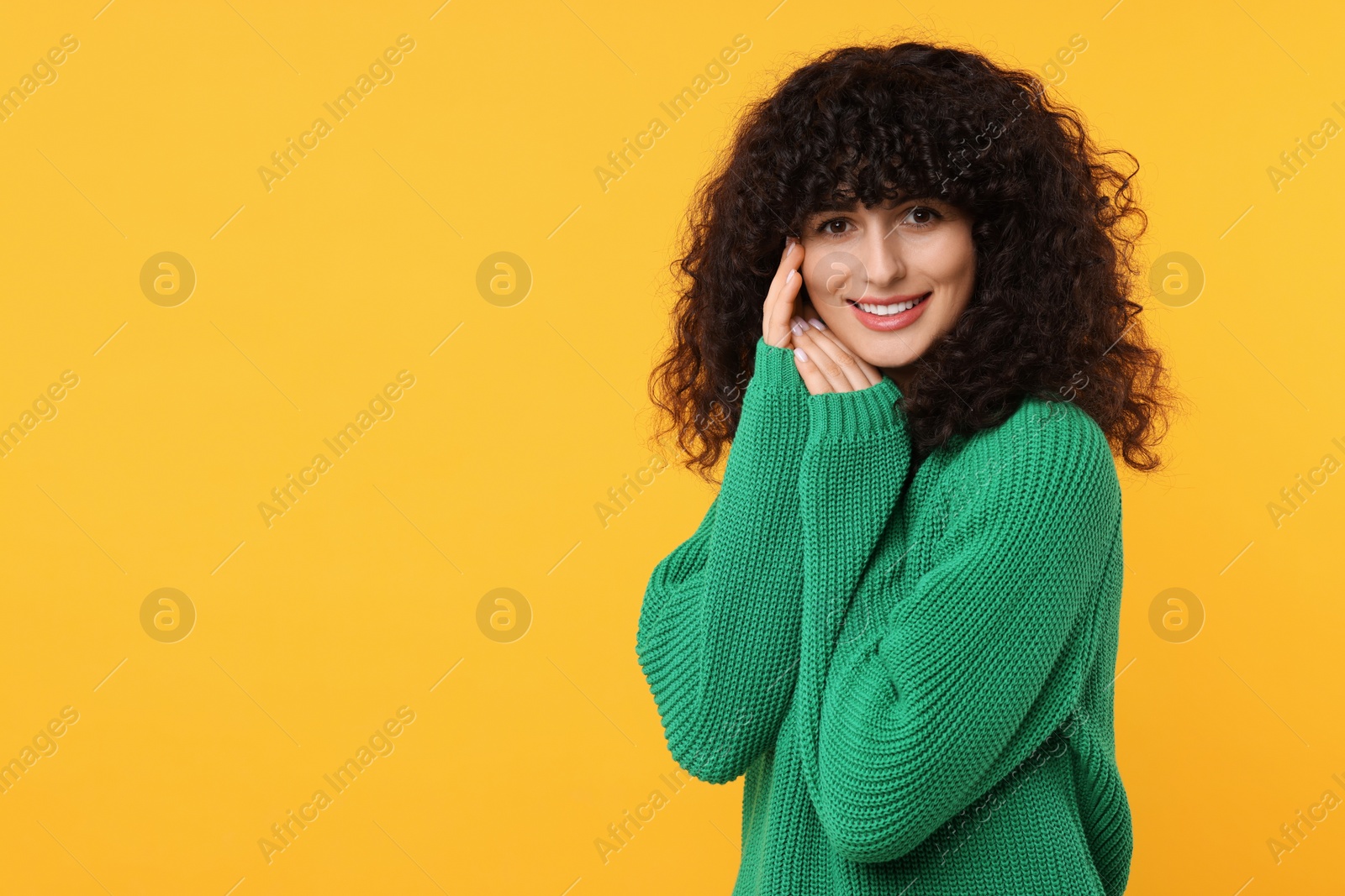 Photo of Happy young woman in stylish green sweater on yellow background, space for text