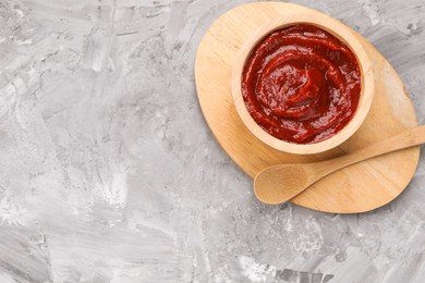 Photo of Organic ketchup in wooden bowl and spoon on grey textured table, top view with space for text. Tomato sauce
