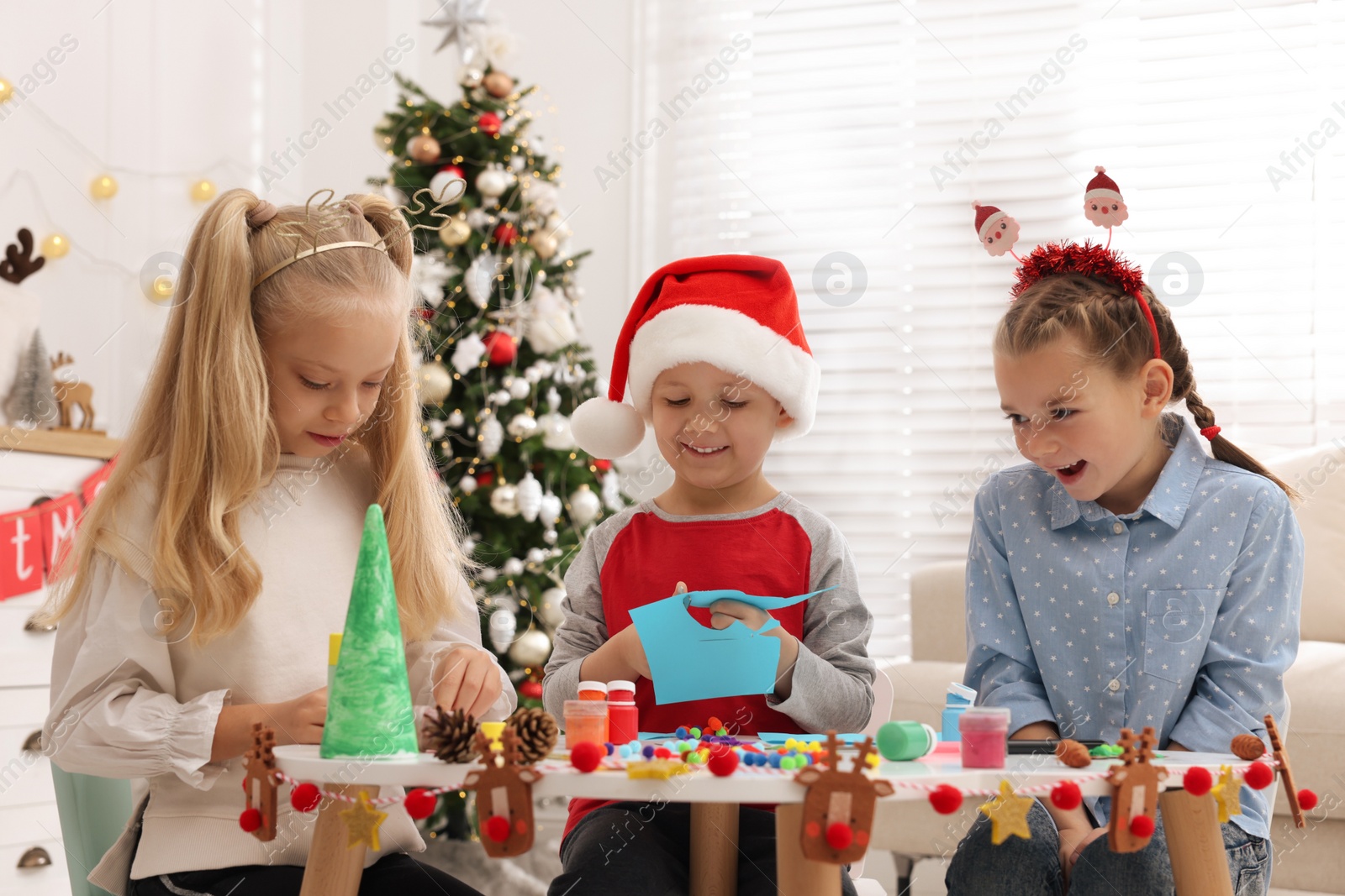 Photo of Cute little children making Christmas crafts at table in decorated room