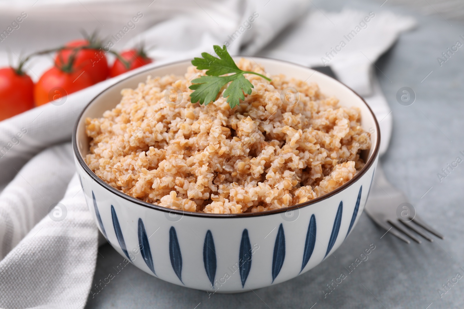 Photo of Tasty wheat porridge with parsley in bowl on grey table, closeup