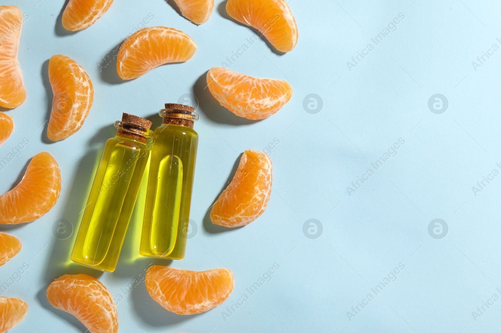 Photo of Aromatic tangerine essential oil in bottles and citrus fruits on light blue table, flat lay. Space for text