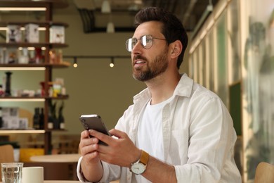 Handsome man with smartphone at table in cafe