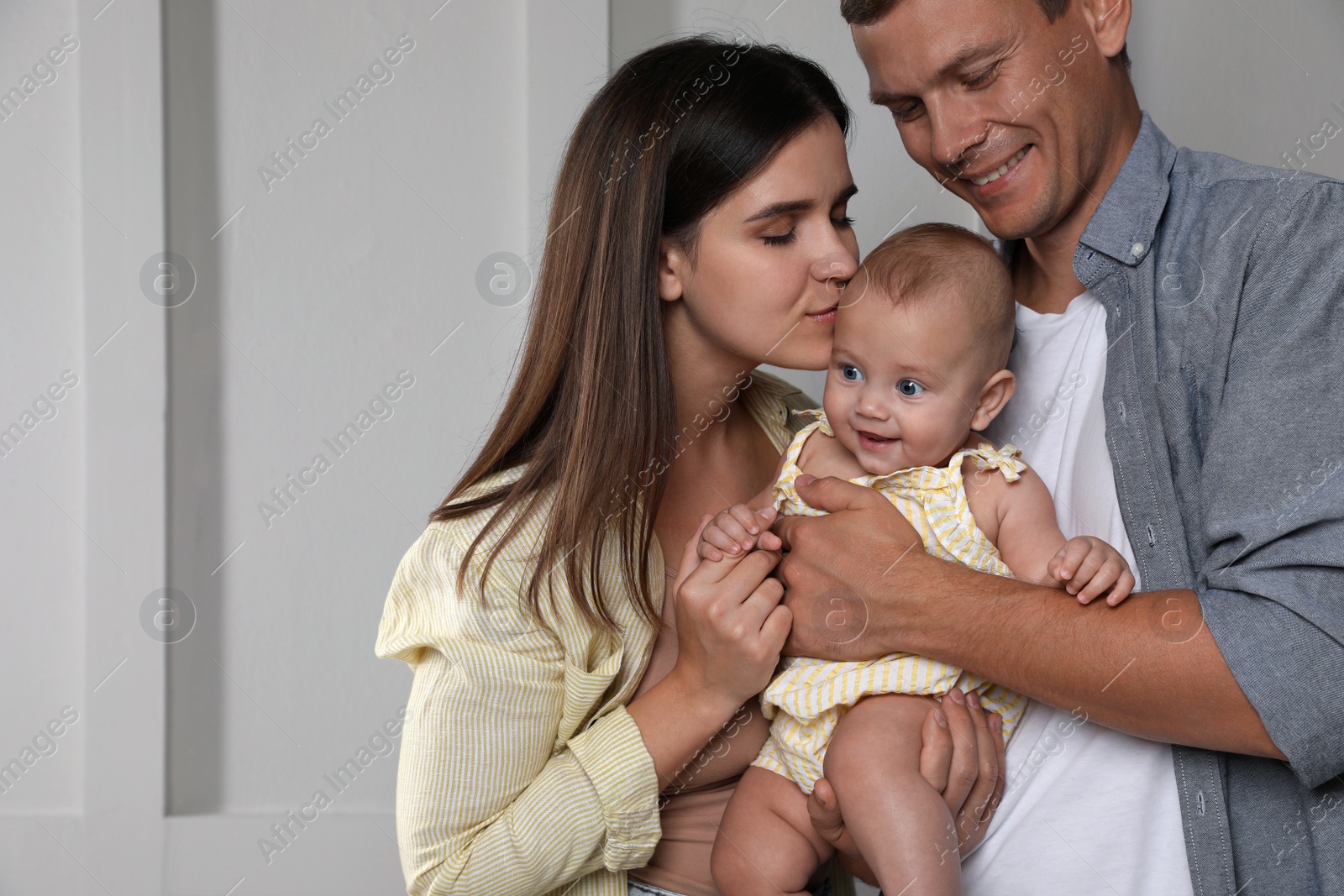 Photo of Happy family. Couple with their cute baby near light wall