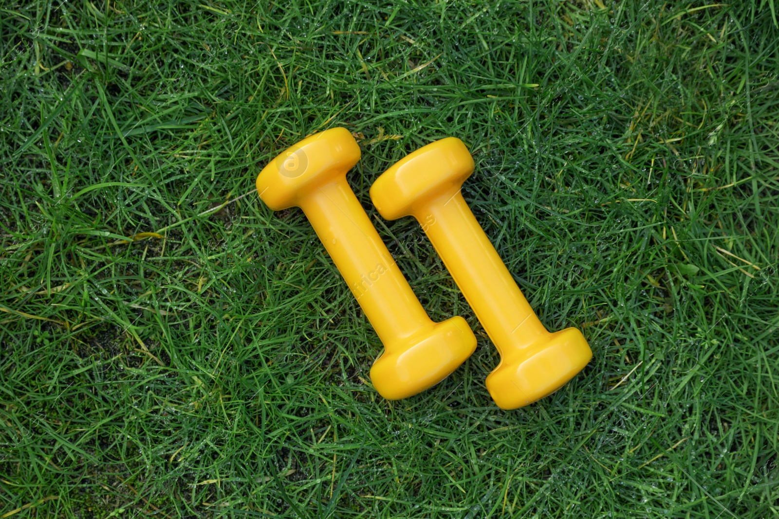 Photo of Yellow dumbbells on green grass, top view. Morning exercise