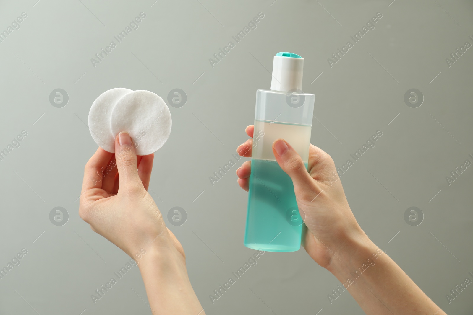 Photo of Woman holding makeup remover and cotton pads on light grey background, closeup