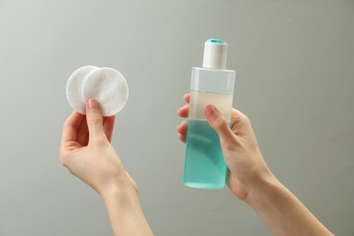 Woman holding makeup remover and cotton pads on light grey background, closeup