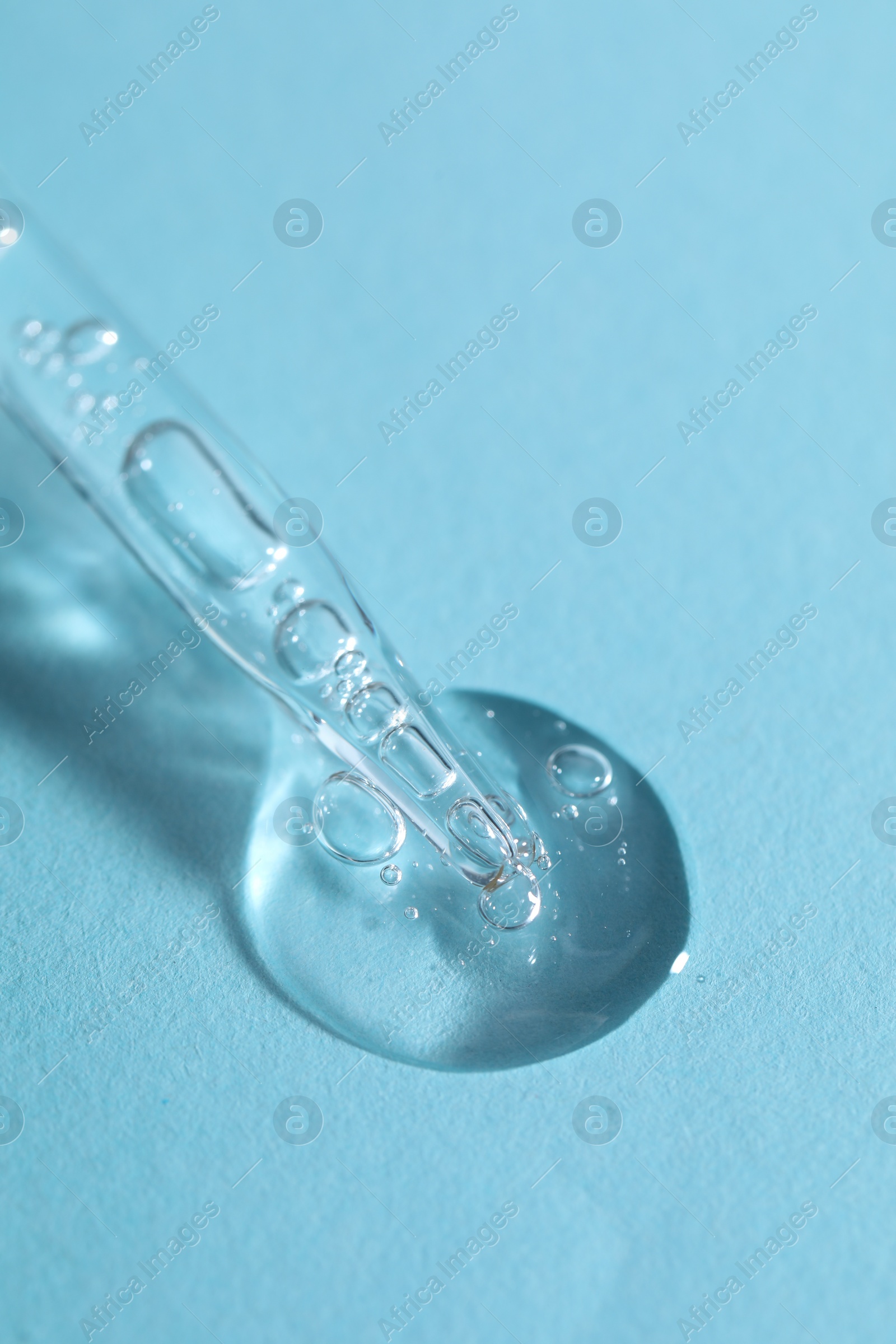 Photo of Glass pipette and transparent liquid on light blue background, closeup