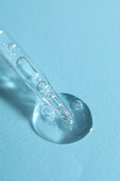 Photo of Glass pipette and transparent liquid on light blue background, closeup