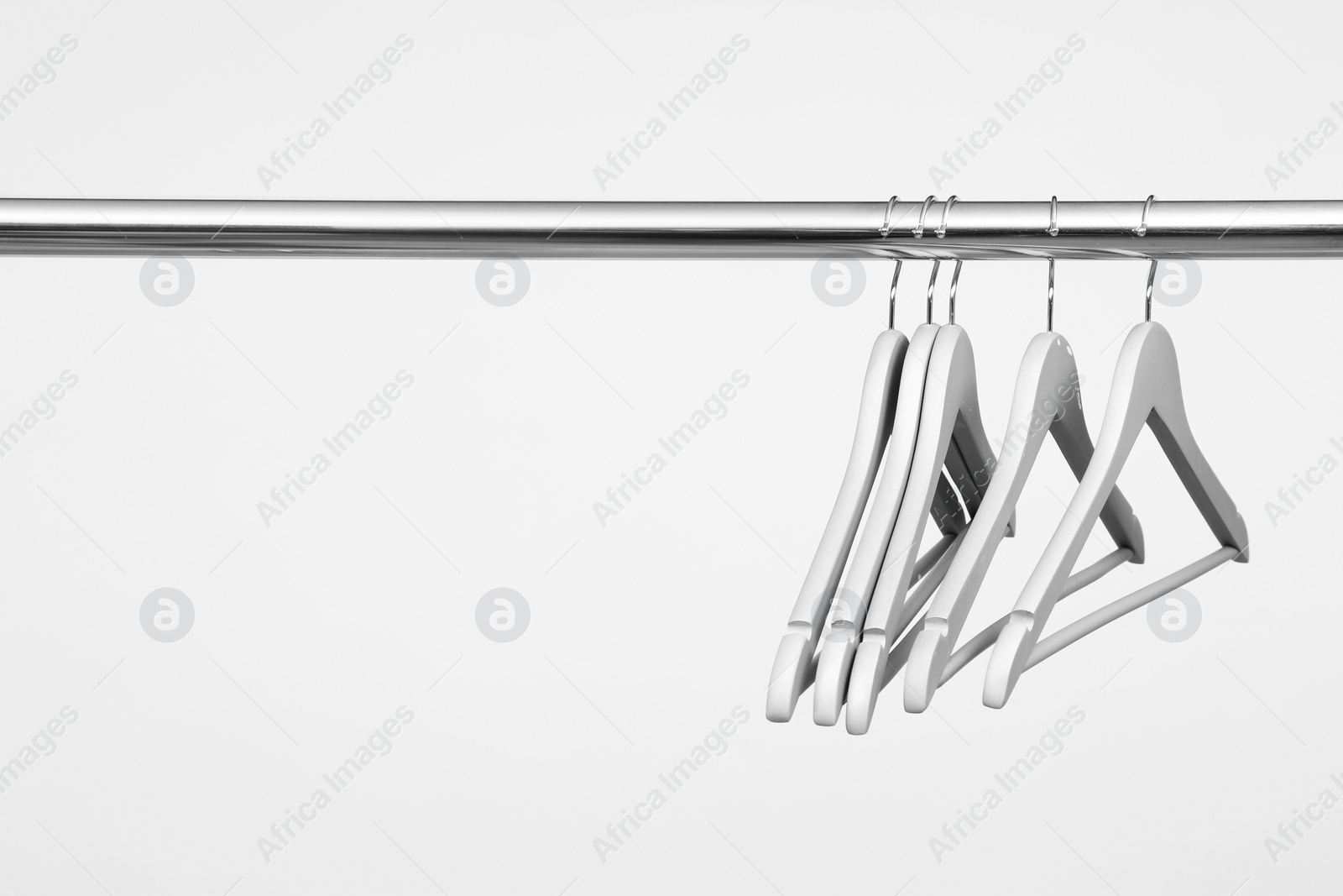 Photo of Empty clothes hangers on metal rail against light background. Space for text