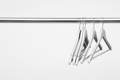 Photo of Empty clothes hangers on metal rail against light background. Space for text