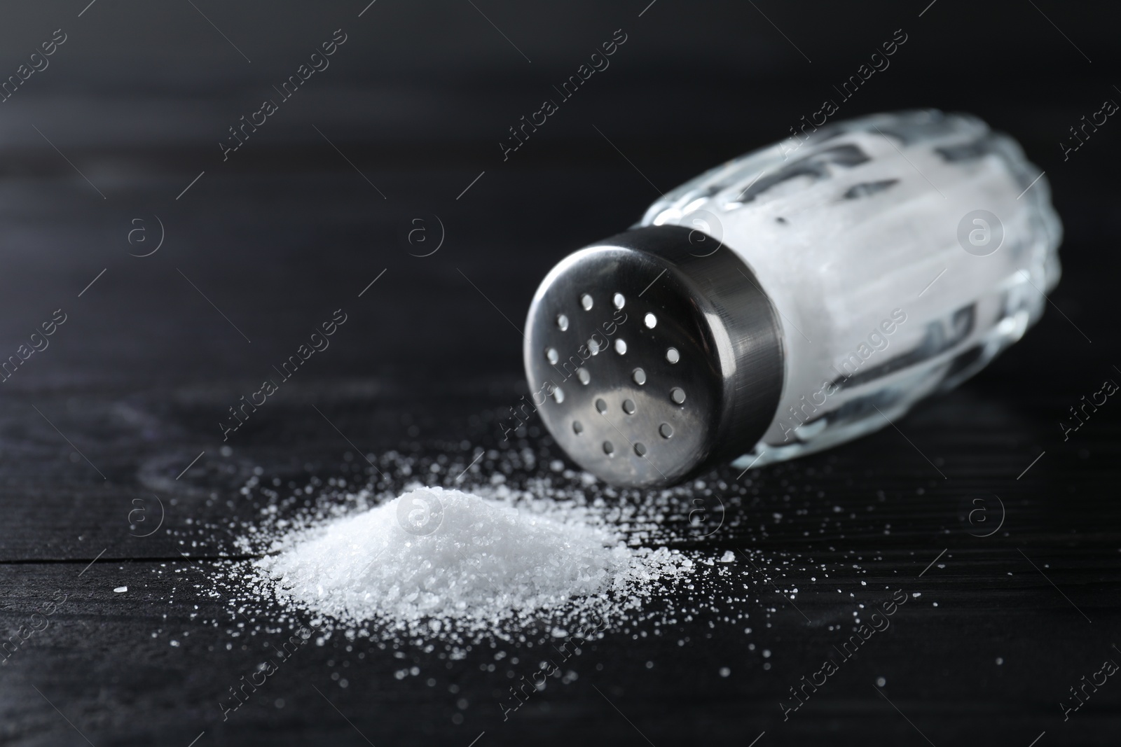 Photo of Organic salt in glass shaker on black wooden table, closeup. Space for text