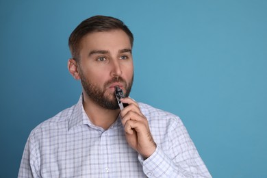 Man using electronic cigarette on light blue background. Space for text