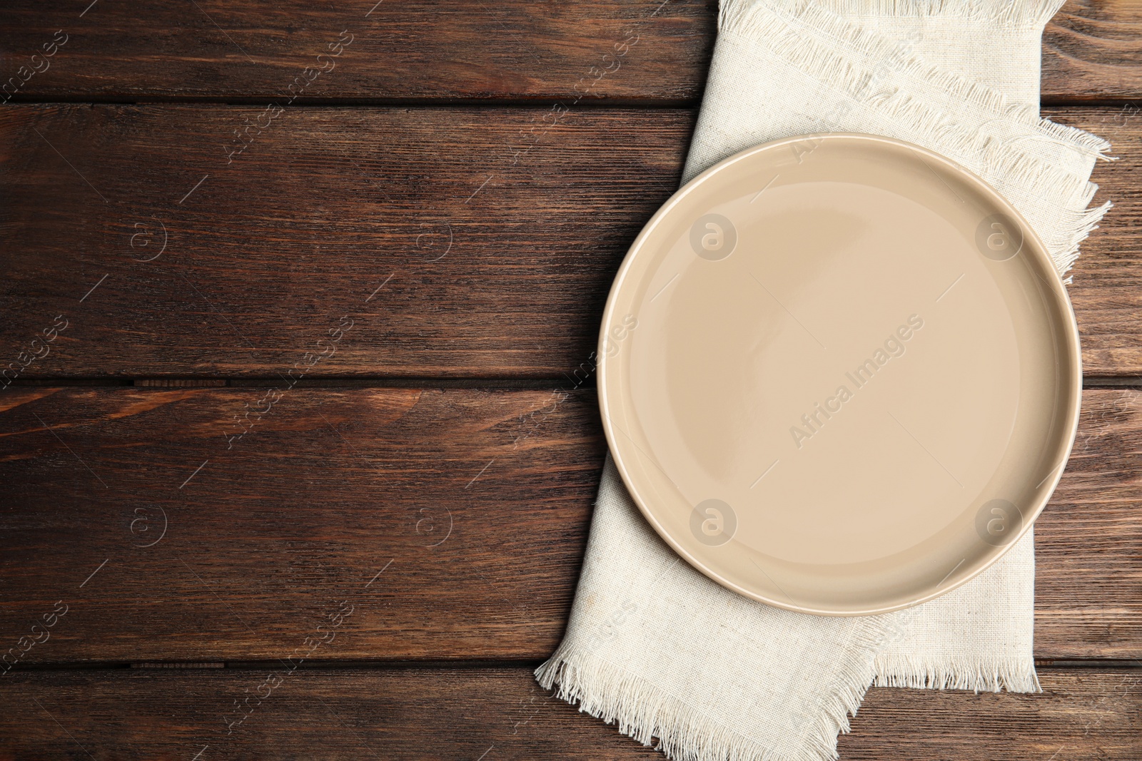 Photo of Empty plate and napkin on wooden table, top view. Space for text