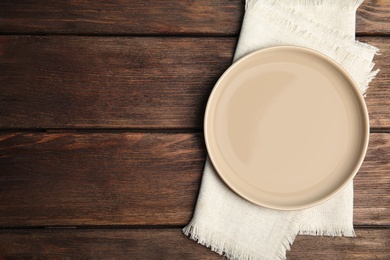 Photo of Empty plate and napkin on wooden table, top view. Space for text