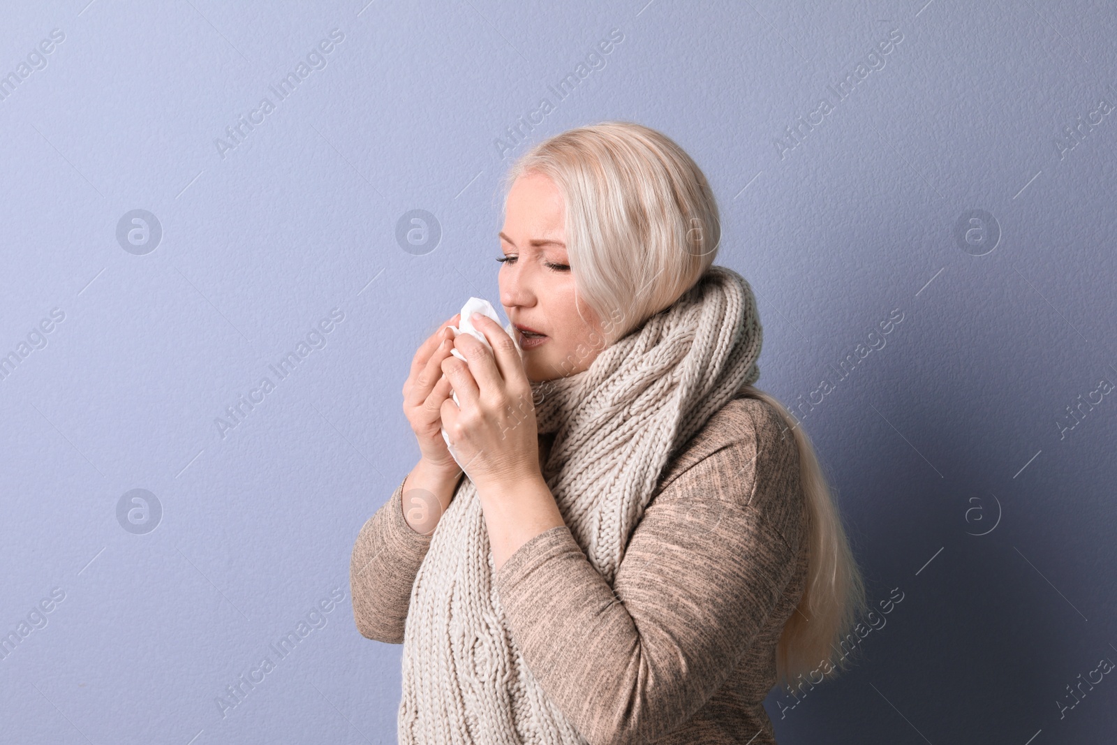 Photo of Mature woman with tissue suffering from cold on color background