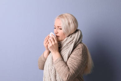 Mature woman with tissue suffering from cold on color background