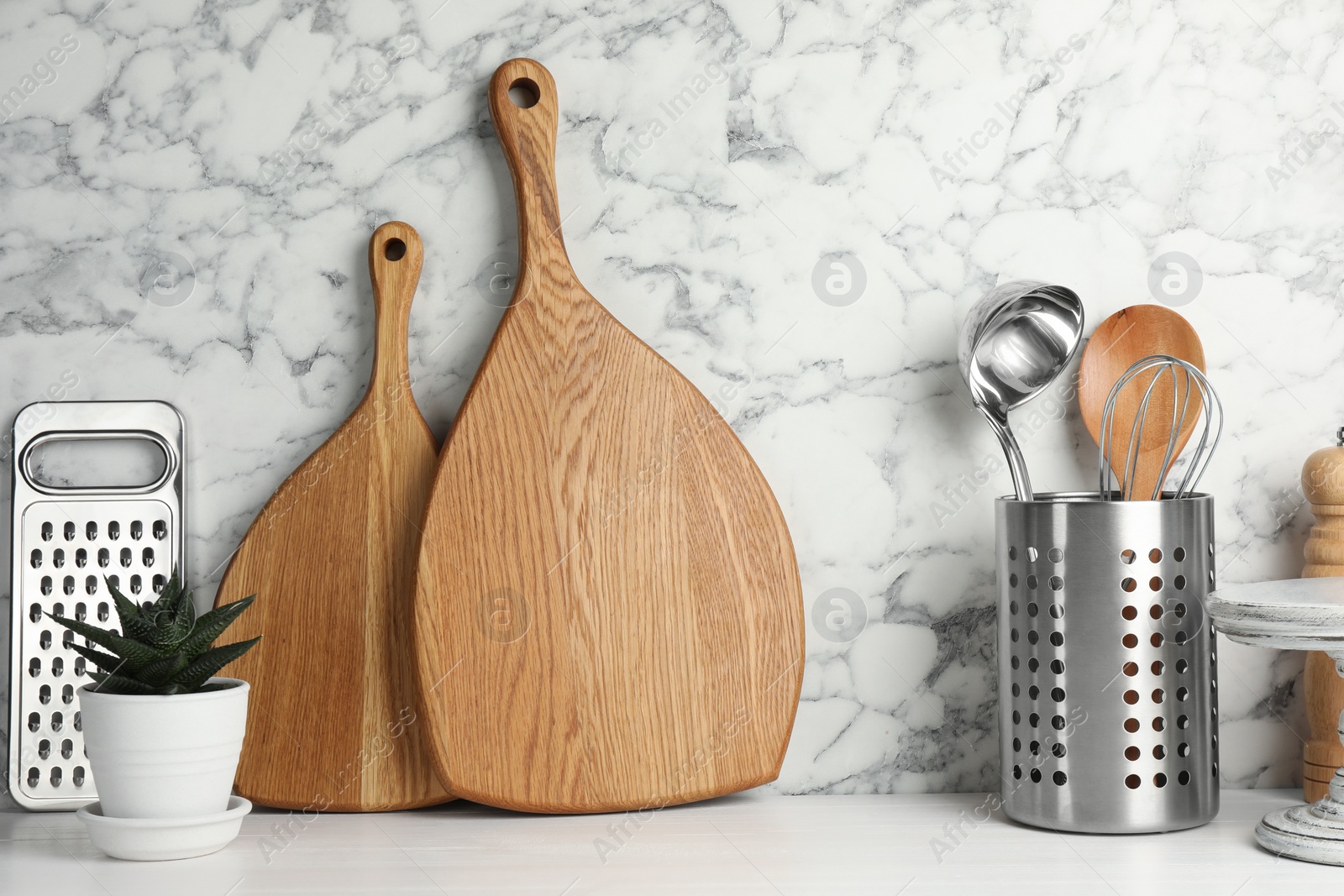 Photo of Wooden cutting boards, kitchen utensils and houseplant on white table near marble wall