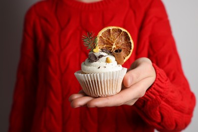 Woman holding tasty Christmas cupcake with cream and decor on light background, closeup