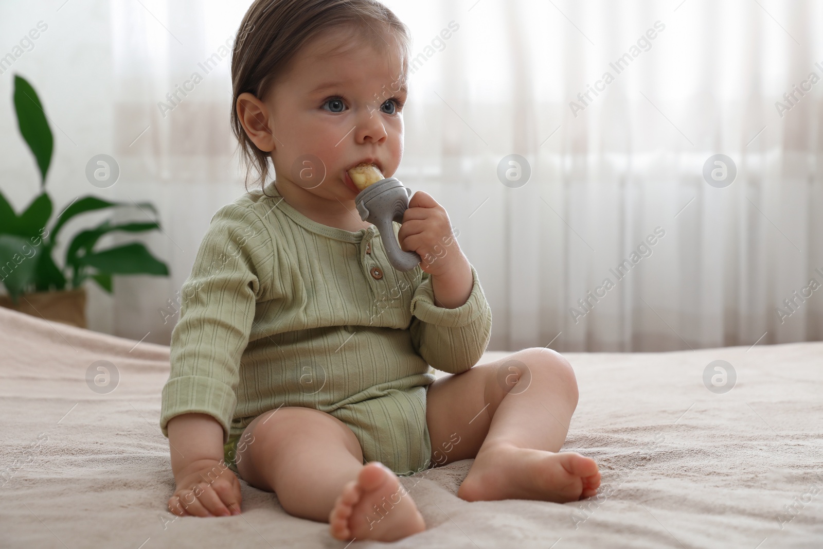 Photo of Cute baby girl with nibbler on bed at home