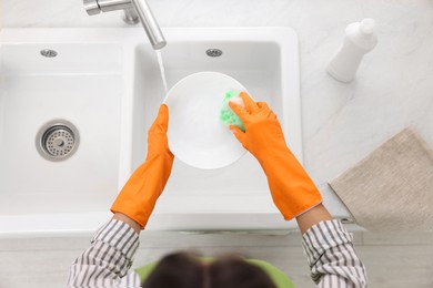 Woman washing plate above sink in modern kitchen, top view