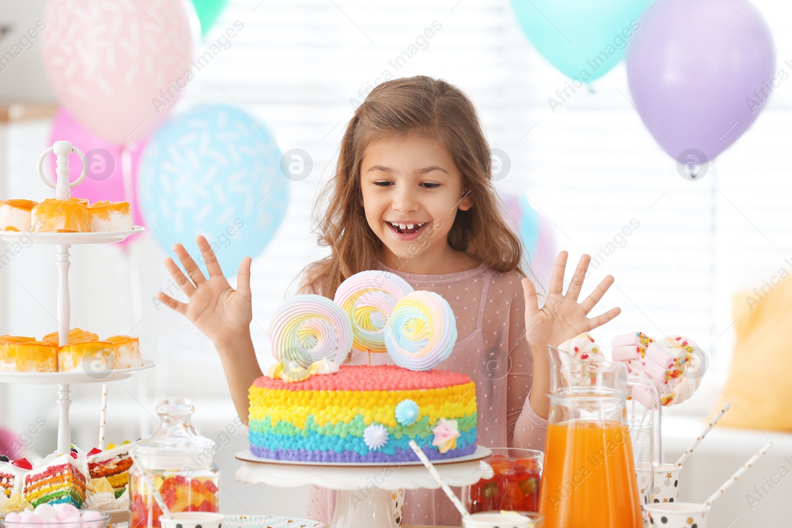 Photo of Happy girl at table with treats in room decorated for birthday party