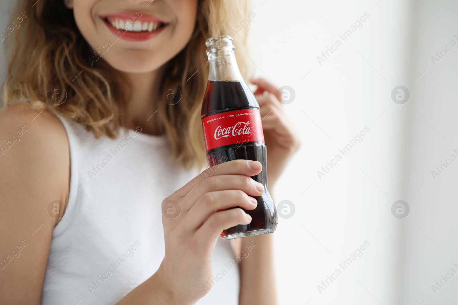 Photo of MYKOLAIV, UKRAINE - NOVEMBER 28, 2018: Young woman with bottle of Coca-Cola indoors, closeup