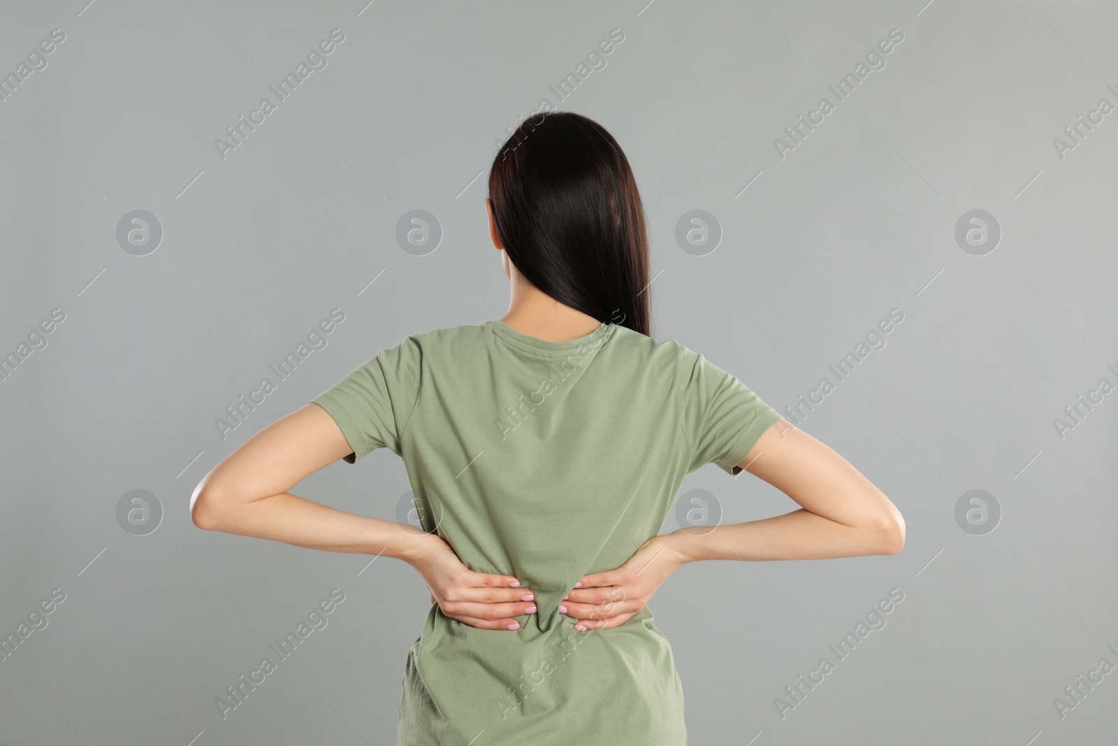 Photo of Woman suffering from lower back pain on light grey background. Visiting orthopedist