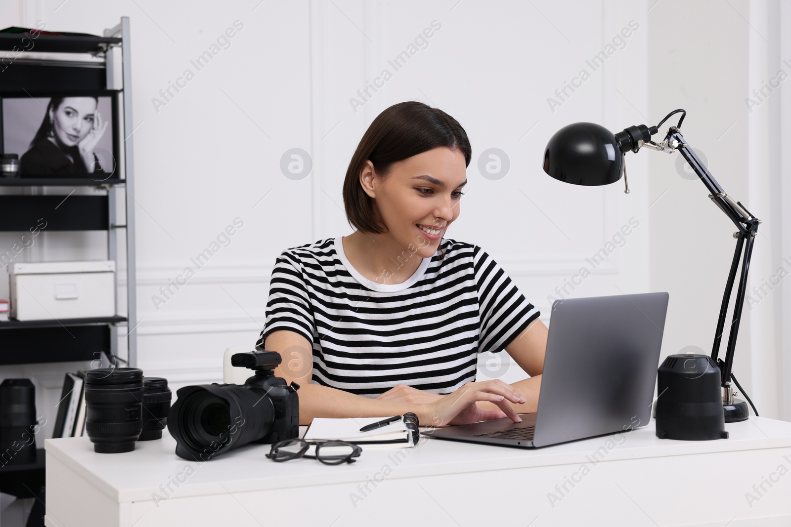 Photo of Young professional photographer with camera working on laptop in modern photo studio