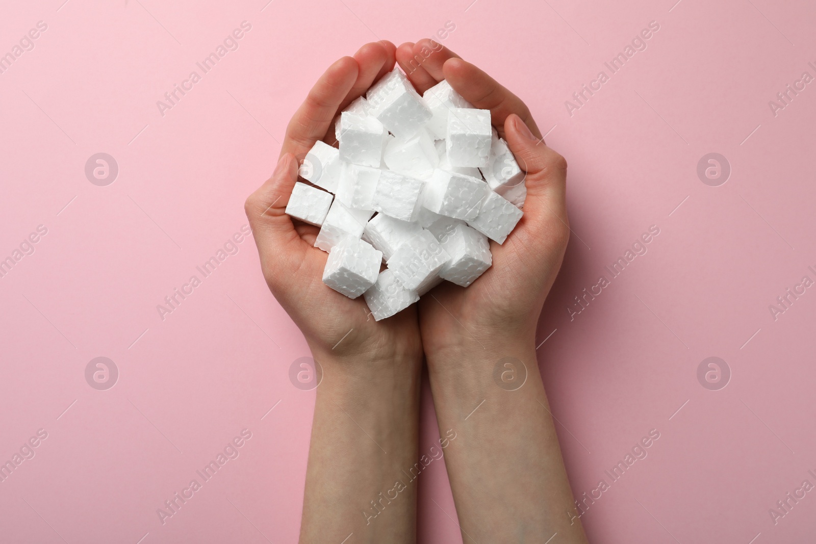 Photo of Woman with handful of styrofoam cubes on pink background, top view