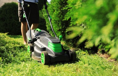 Photo of Man cutting grass with lawn mower in garden on sunny day, closeup
