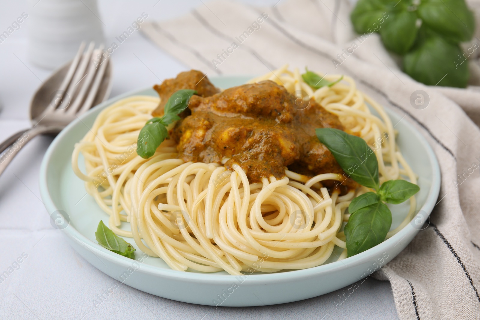 Photo of Delicious pasta and chicken with curry sauce served on white tiled table, closeup