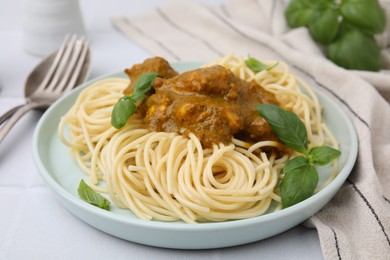 Photo of Delicious pasta and chicken with curry sauce served on white tiled table, closeup