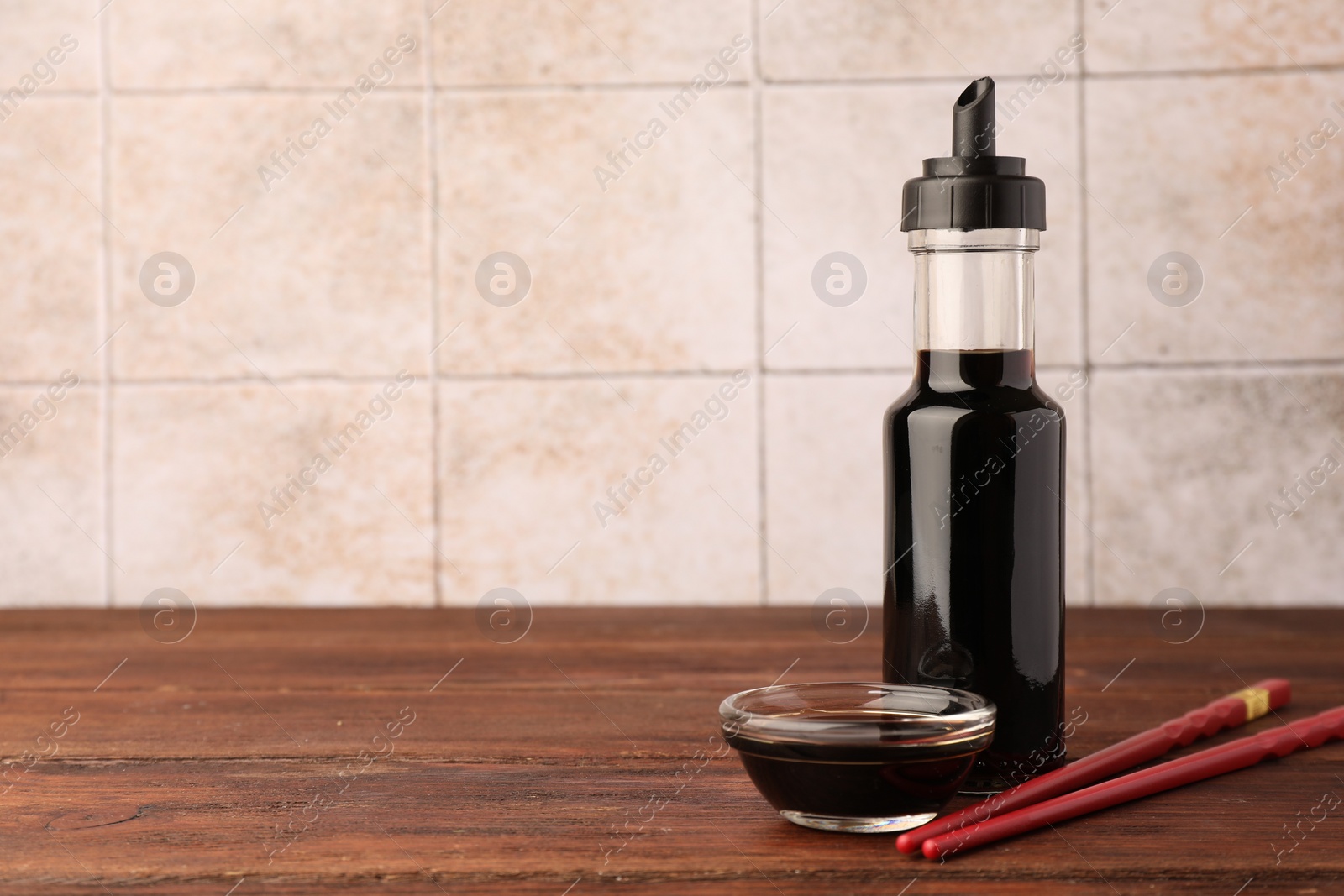 Photo of Bottle, bowl with soy sauce and chopsticks on wooden table. Space for text