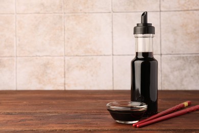 Bottle, bowl with soy sauce and chopsticks on wooden table. Space for text