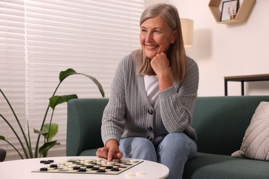 Happy senior woman playing checkers at home