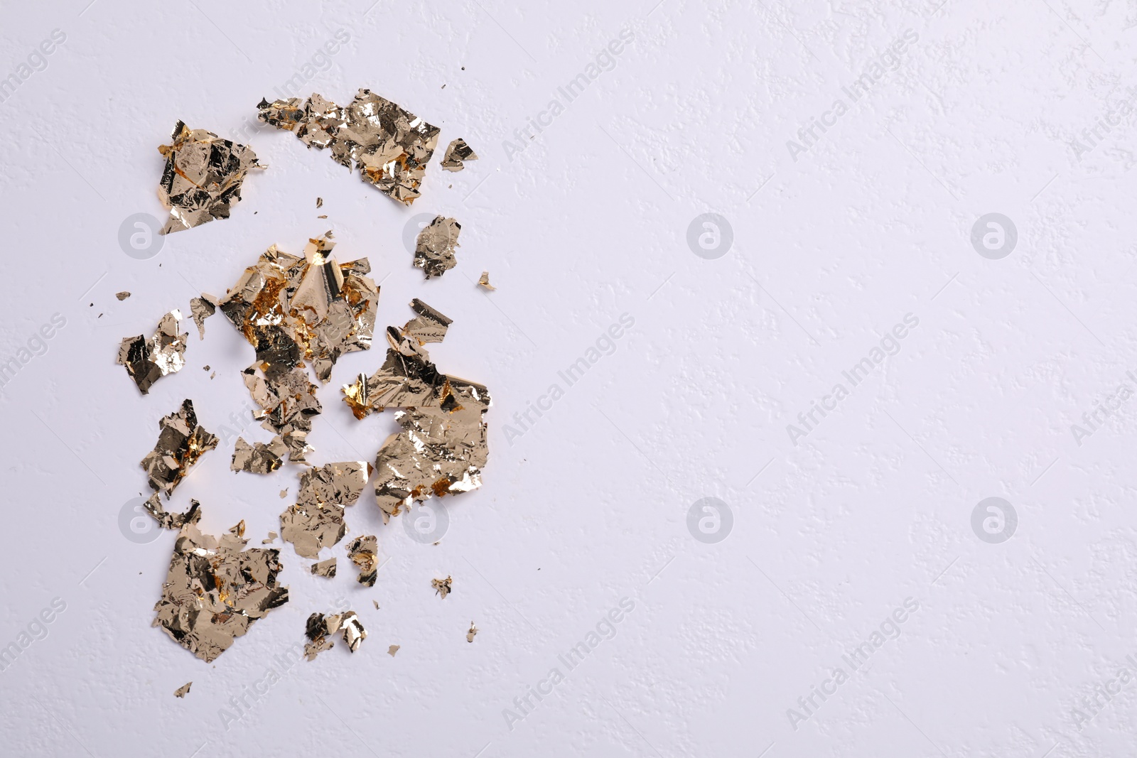 Photo of Many pieces of edible gold leaf on white textured table, flat lay. Space for text