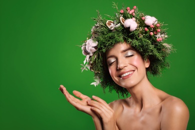 Happy young woman wearing wreath on green background. Space for text