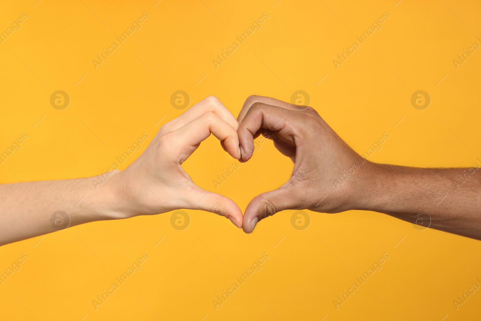 Photo of International relationships. People making heart with hands on orange background, closeup